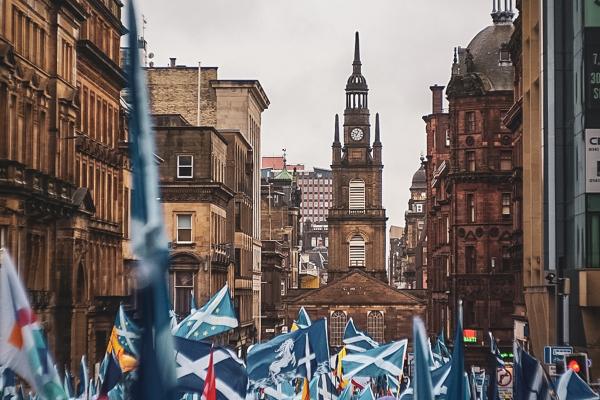 Image of people marching with Scottish flags surrounded by buildings